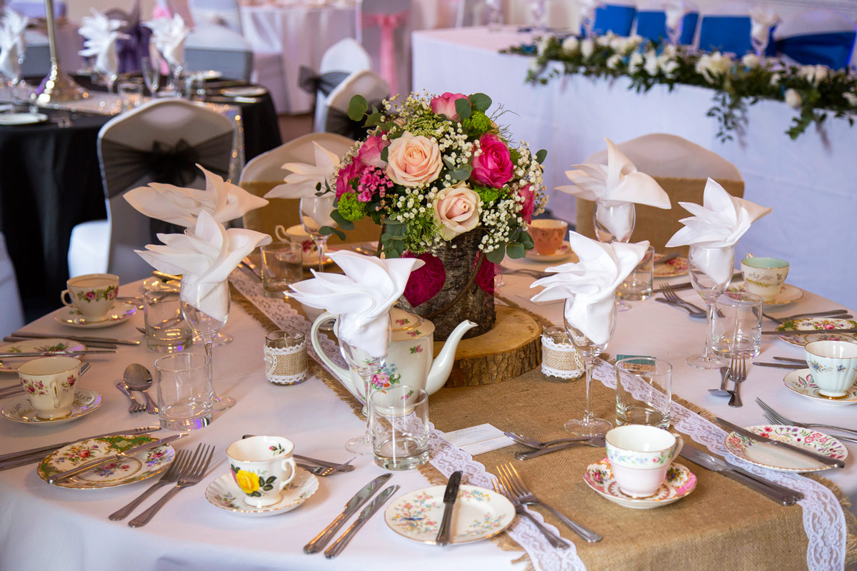 An elaborately decorated table laid out with a china tea set with a centrepiece of fresh flowers