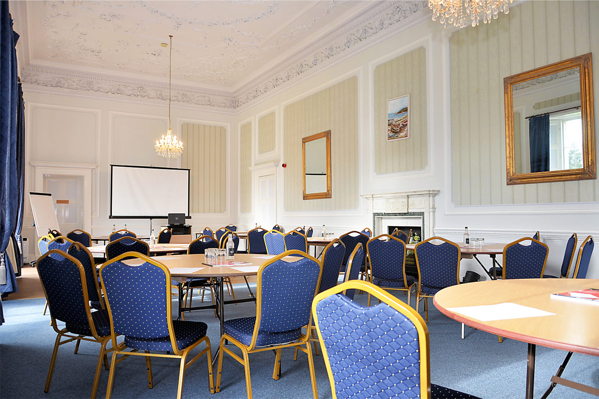A room set up with round tables and chairs, there is a large projector screen situated at the end of the room
