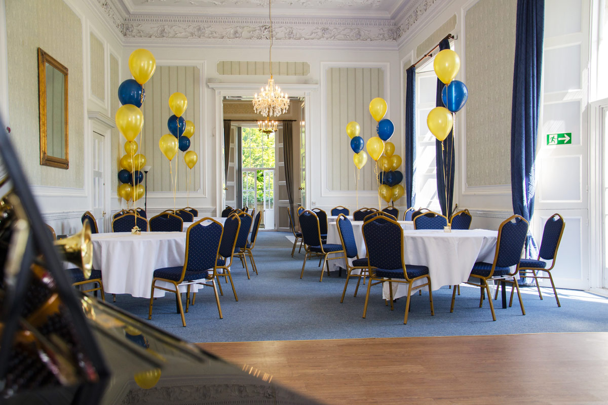 A large room set up with round tables and chairs multi colour balloons rise from each table