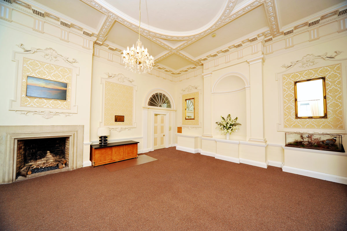 The Grand Entrance Hall, decorated with an ornate plasterwork ceiling, a large fireplace and a chandelier 